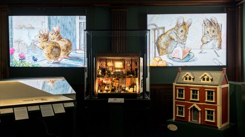 Interior of a room with display cabinets, a dolls' house and projections of mice from 'the Tale of Two Bad Mice' on the walls.